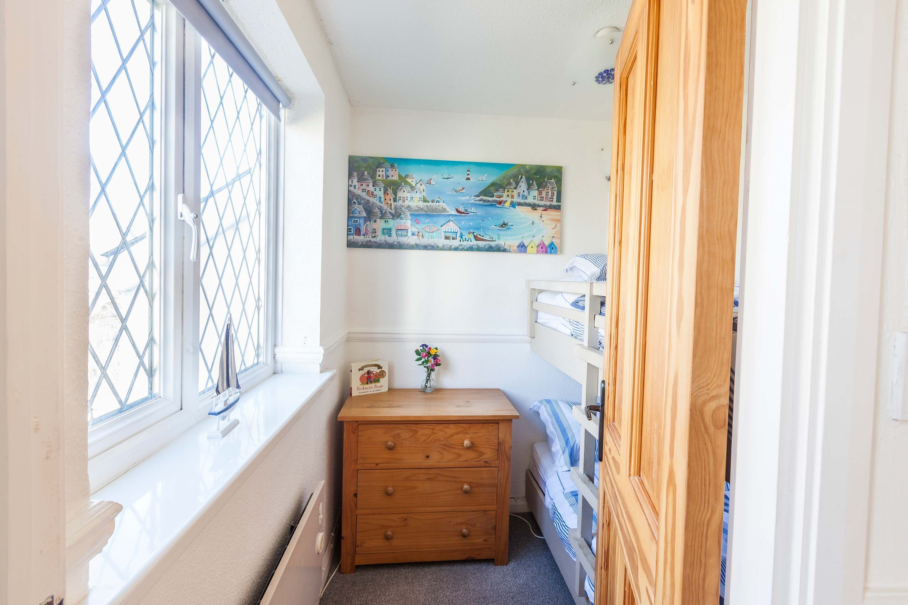 Una habitación estrecha con un aparador de madera, una ventana que ofrece vistas de la costa y un cuadro en la pared.
