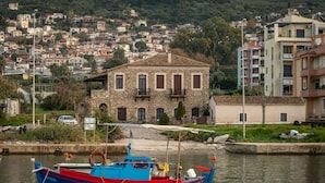 Une ville côtière avec un bâtiment en pierre, un bateau aux couleurs vives et une colline parsemée de maisons.