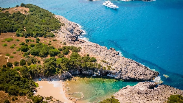 Un paysage côtier caractérisé par une rive rocheuse, des eaux d’un bleu limpide et un yacht.