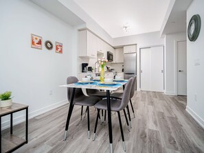 Une cuisine moderne avec des meubles blancs, un réfrigérateur en acier inoxydable et un coin repas avec une table dressée pour quatre personnes.