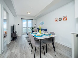 Un espace de repas moderne avec une table dressée pour quatre personnes, un téléviseur et un balcon offrant une vue sur la ville.