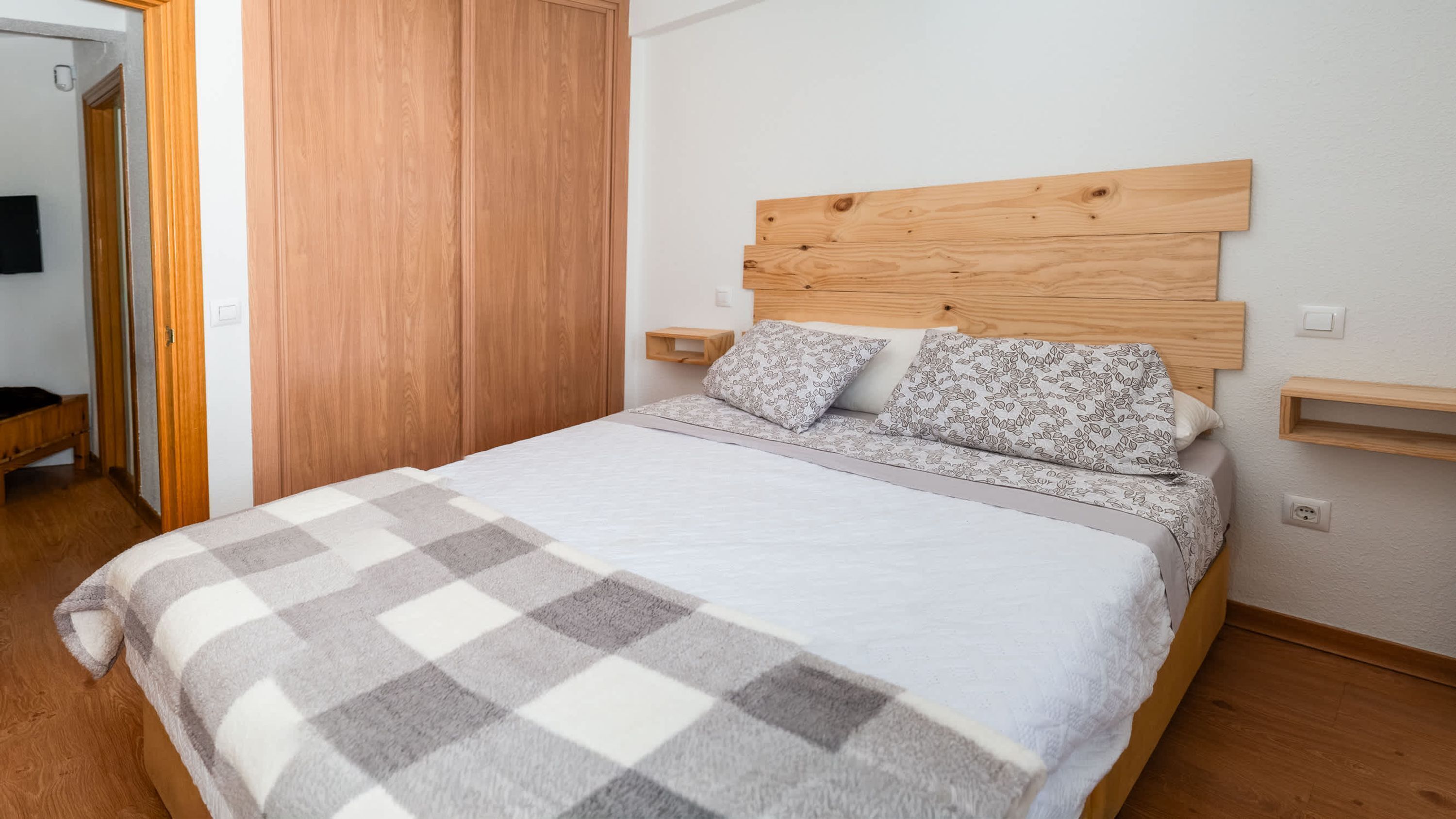 Une chambre à coucher avec une tête de lit en bois, une couverture à carreaux, deux coussins à motifs et une table de chevet.