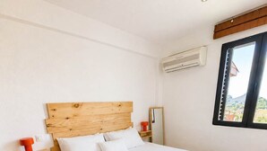 Quarto bem arrumado com cabeceira de madeira, cama com lençóis brancos, manta azul e janela com vista.