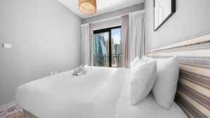 A hotel room with a large bed, a view of the city through a window, a hanging light fixture, and a framed picture on the wall. - Free Housekeeping Visits During Your Stay - Stayshort - 1 Bed in Business Bay With Modern Amenities That Sleeps 4 (Dubai)