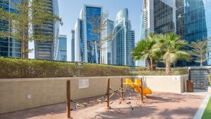 A playground area with climbing structures, a yellow slide, and palm trees. - Free Housekeeping Visits During Your Stay - Stayshort - 1 Bed in Business Bay With Modern Amenities That Sleeps 4 (Dubai)