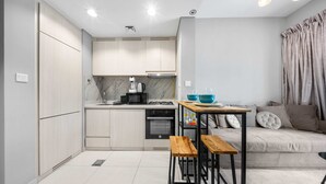 A compact kitchen with modern appliances, a dining area with stools, and a sofa with cushions. - Free Housekeeping Visits During Your Stay - Stayshort - 1 Bed in Business Bay With Modern Amenities That Sleeps 4 (Dubai)