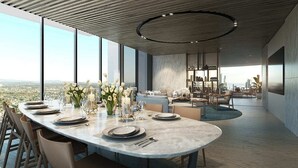 A modern dining area with a large table set for a meal, a kitchen in the background, and a city view.