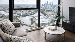 A modern living room with a large window, a sofa, a round coffee table, a potted plant, and a TV stand.