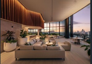 A modern rooftop lounge with a sofa, chairs, and tables, large windows offering a city view. - 2BR Resort Style Apartment with Panoramic Views (Broadbeach)
