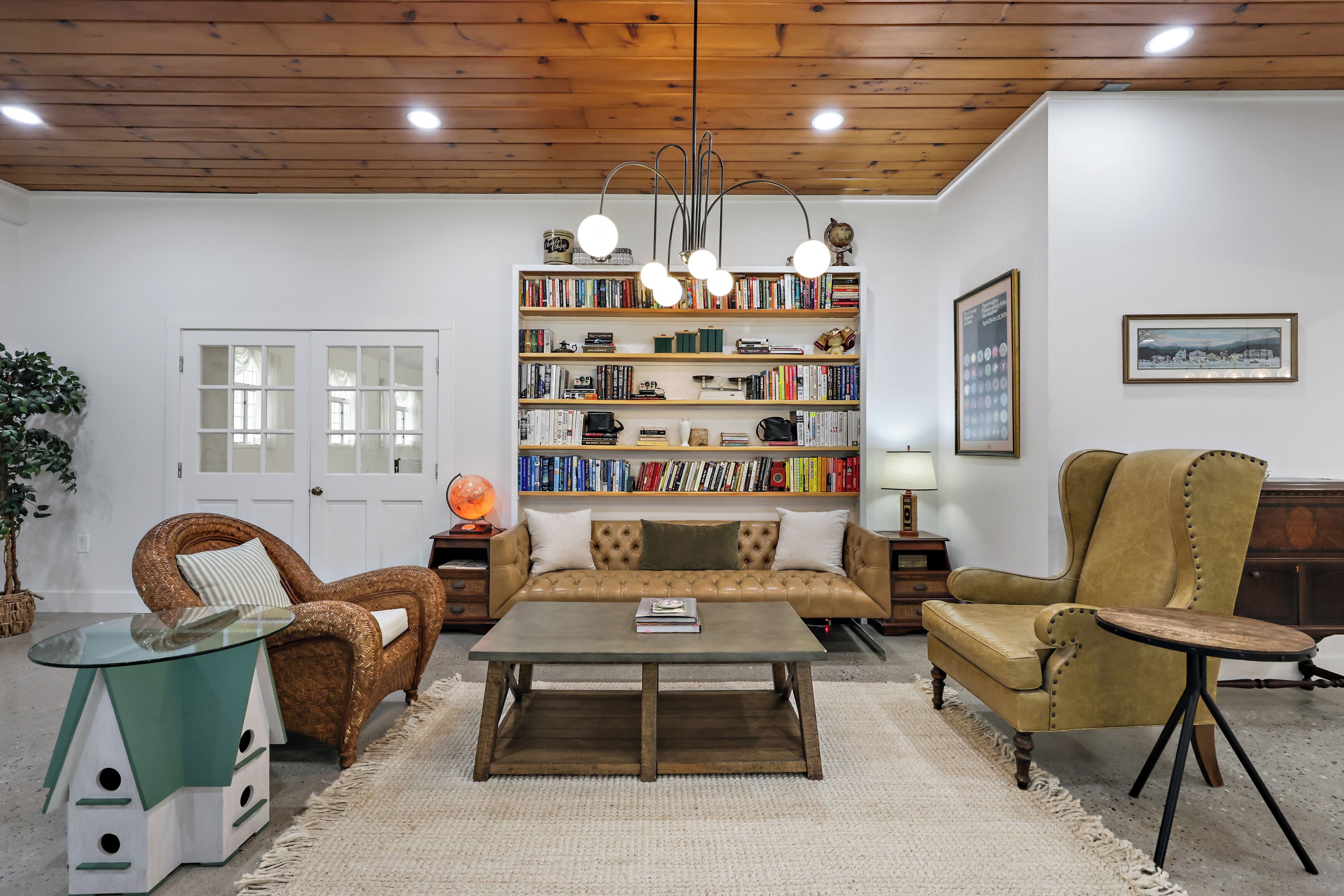 A living room with a sofa, armchairs, a coffee table, a bookshelf, and a wooden ceiling.