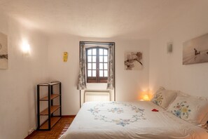 Une chambre à coucher avec un lit, une fenêtre avec des rideaux, un radiateur, une étagère et des œuvres d’art murales.