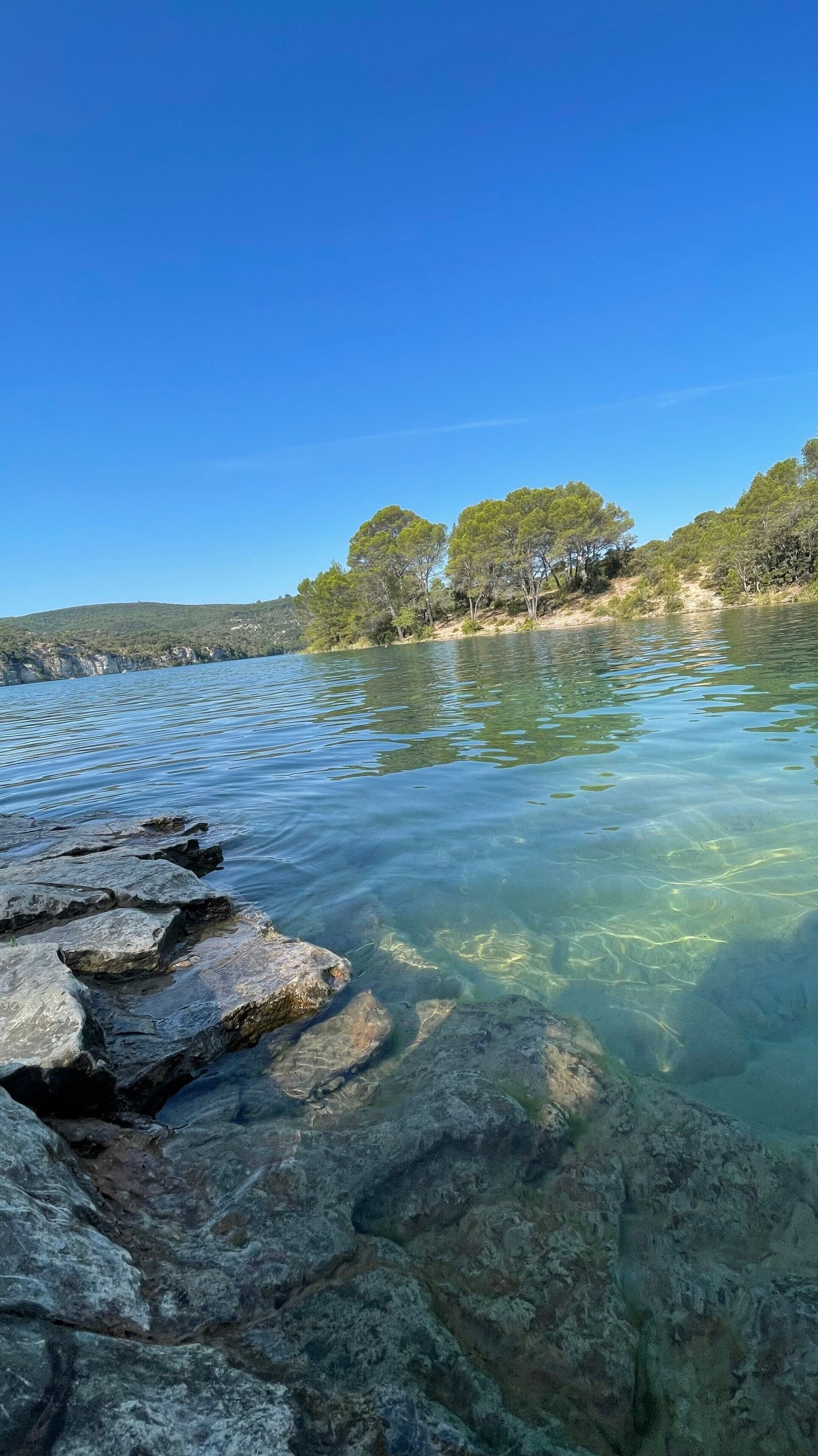 Un lac aux eaux claires, avec des rochers visibles et des arbres en arrière-plan.