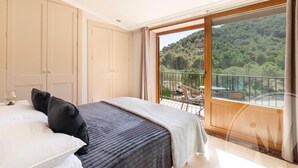 A bedroom with a large bed, a wardrobe, and a balcony with a view of a forested hillside. - La Manga Club Atalayas II Villa 616 (Cartagena)