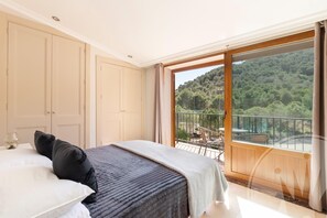 Un dormitorio con una cama grande, un armario y un balcón con vista a una ladera boscosa.