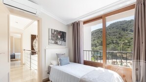 A bedroom with a bed, a window with a view of a forest, and a painting on the wall. - La Manga Club Atalayas II Villa 616 (Cartagena)