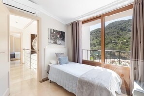 A bedroom with a bed, a window with a view of a forest, and a painting on the wall. - La Manga Club Atalayas II Villa 616 (Cartagena)