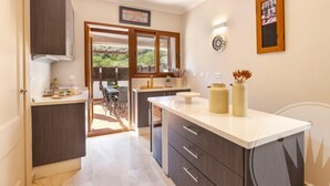 A modern kitchen with dark cabinetry, a white countertop, and a view to an outdoor dining area. - La Manga Club Atalayas II Villa 616 (Cartagena)