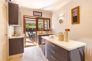 Una cocina moderna con armarios oscuros, encimera blanca y vistas a un área de comedor exterior.