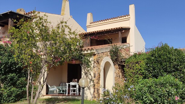 Ein zweistöckiges Haus mit Terrasse, steinbogigem Eingang und einem Garten.