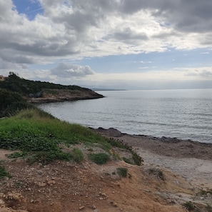 Eine Küstenlandschaft mit felsiger Küste, einer grasbewachsenen Fläche und einem entfernten Blick auf das Meer unter bewölktem Himmel.