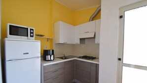 A compact kitchen with a refrigerator, microwave, coffee maker, and gas stove. - Apartment Faro in Budoni (Budoni)
