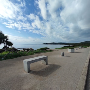 A paved walkway with a bench, a view of the sea, and distant hills. - House Gavina 2 Seaside Alghero (Fertilia)