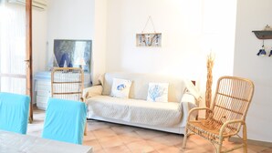 A living room with a sofa, two wicker chairs, a dining table, and a hanging artwork. - House Gavina 2 Seaside Alghero (Fertilia)