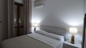 A hotel room with a bed, two bedside tables with lamps, an air conditioning unit, and a curtain. - House Gavina 2 Seaside Alghero (Fertilia)