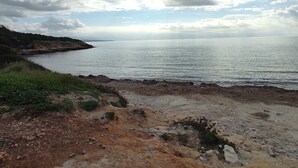 A coastal landscape with a rocky shoreline, a body of water, and a distant landmass under a cloudy sky. - House Gavina 2 Seaside Alghero (Fertilia)