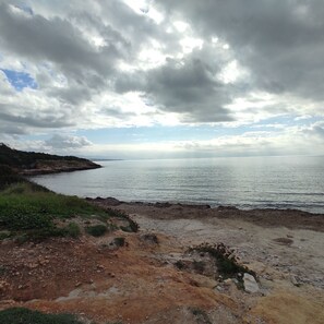 A coastal landscape with a rocky shoreline, a body of water, and a distant landmass under a cloudy sky. - House Gavina 2 Seaside Alghero (Fertilia)