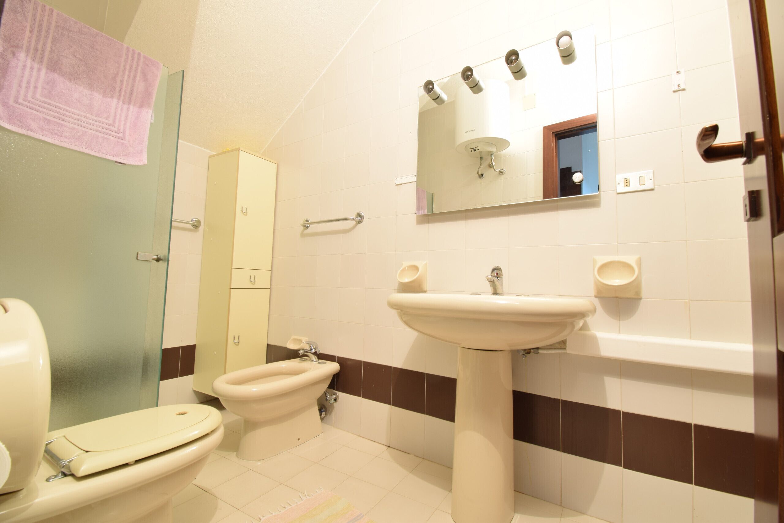 Un baño con inodoro, bidé, lavamanos y espejo.
