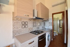 A kitchen with a gas stove, oven, washing machine, and a tiled backsplash. - Casa Chiara Balcony, Budoni (Budoni)