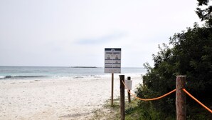 Ein Strand mit einem Wegweiser, einem Holzzaun und einer Seilsperre.