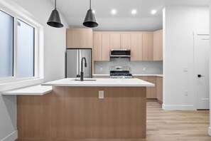 Une cuisine moderne dotée d’un îlot central, d’appareils électroménagers en acier inoxydable et de luminaires suspendus.