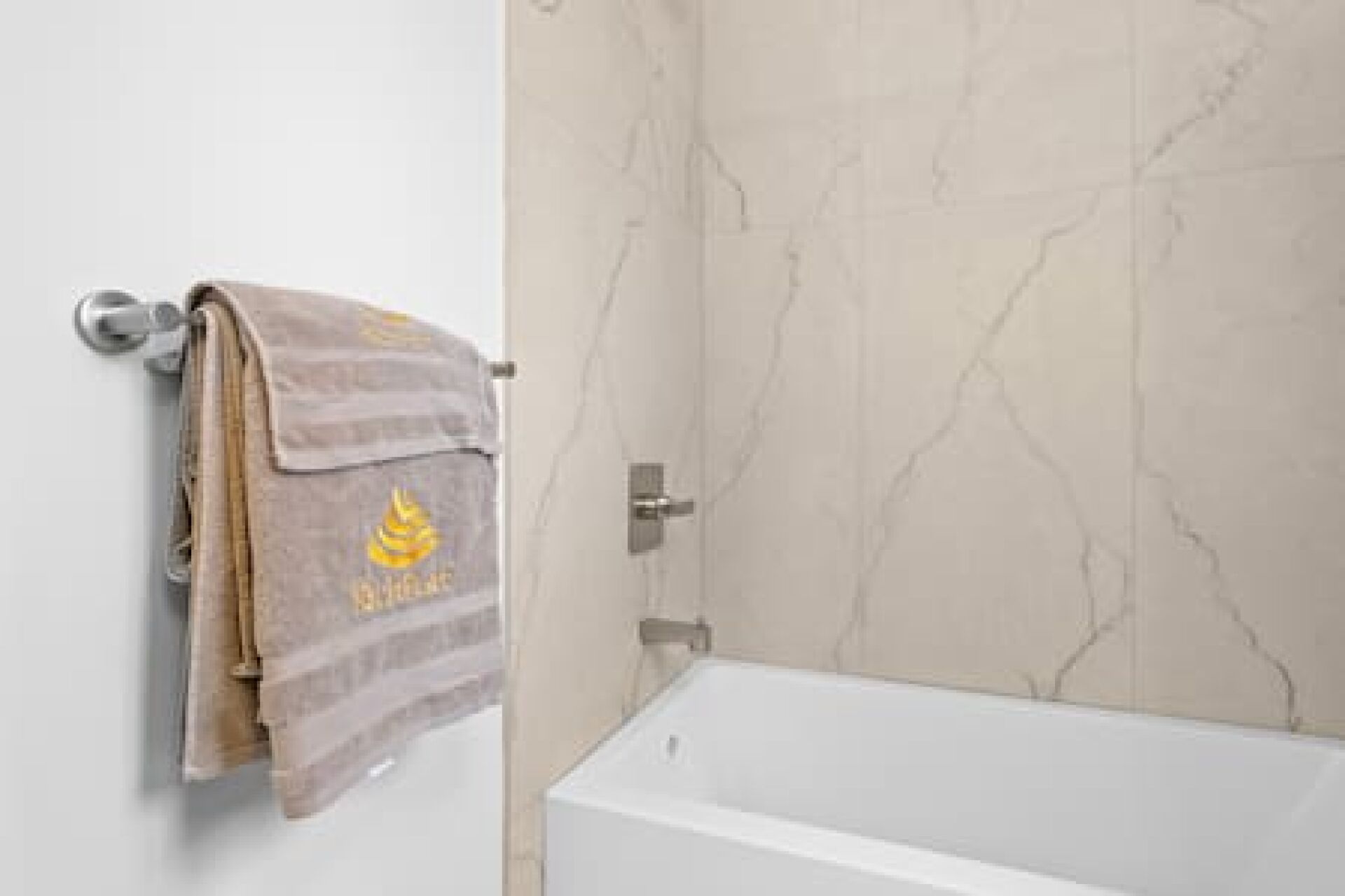 A bathroom with a white bathtub, a towel rack with a towel, and a marble wall.