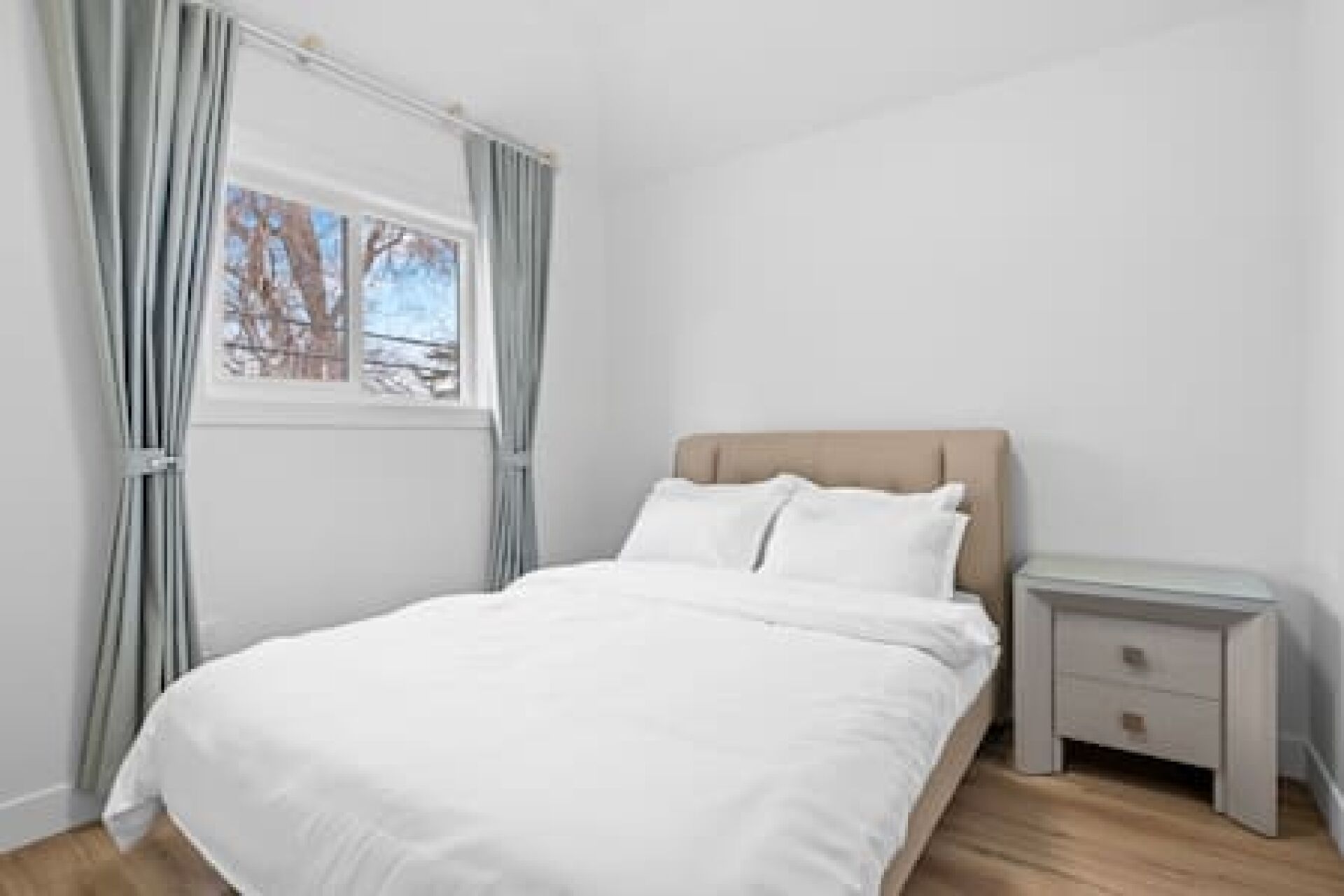 Une chambre à coucher avec un lit, une table de chevet, une fenêtre avec des rideaux et une vue sur les arbres.