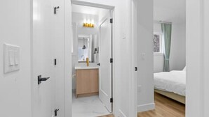 A hotel room with a bed, a bathroom with a mirror, and a hallway leading to another room. - "Avanta" with free parking near UofC (Calgary)