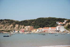 A coastal town with buildings along the shore, boats in the water, and a hilly backdrop.