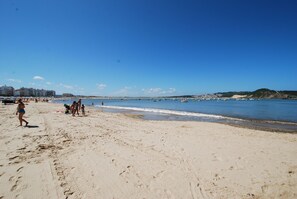 En strand med folk som promenerar, en sandstrand och en klarblå himmel.