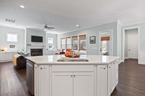 A spacious kitchen with a large island, white cabinetry, a fireplace, and a ceiling fan. - Carolina Cottage in Beau Coast w/Community Pool (Beaufort)