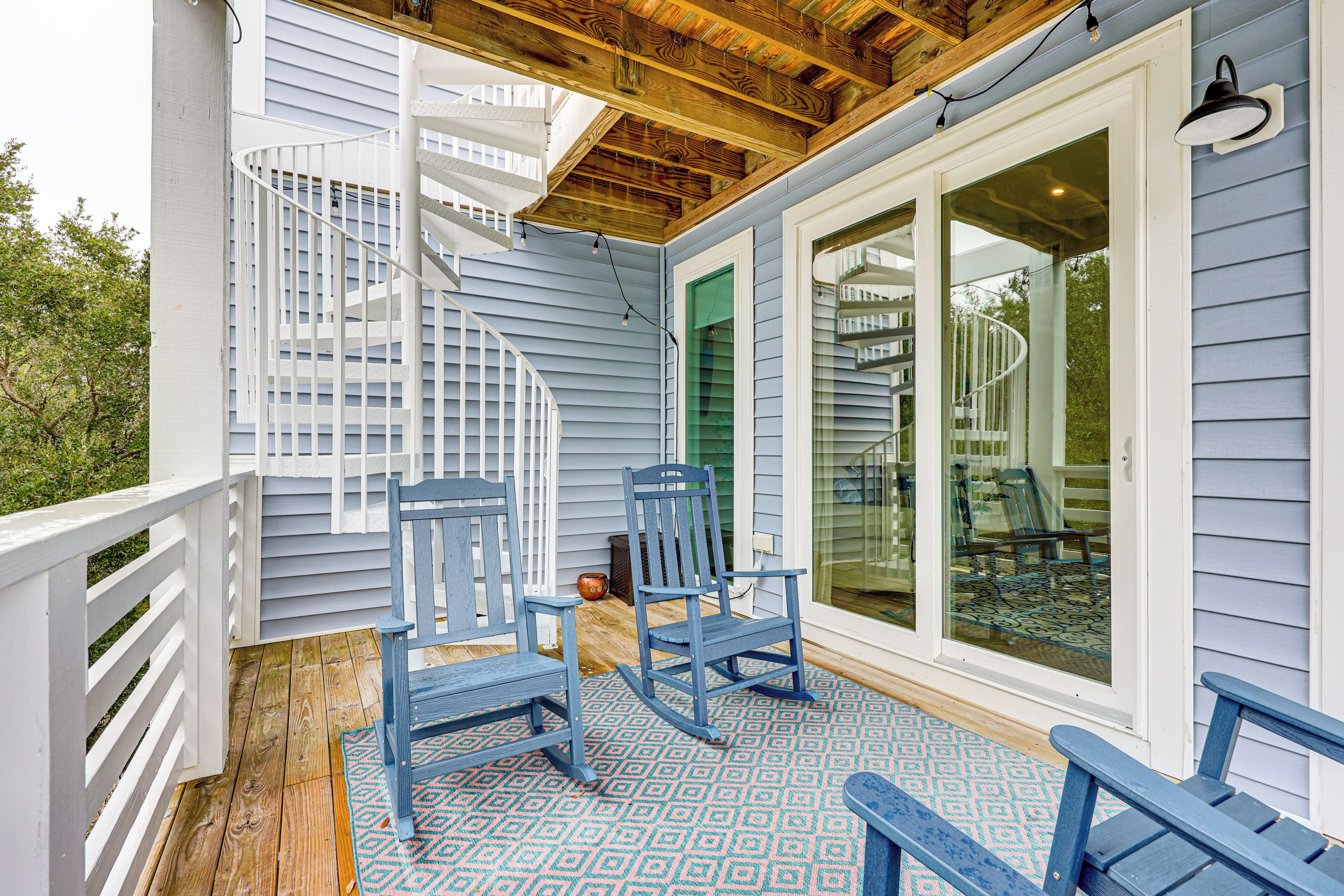A covered porch with blue chairs, a wooden deck, and a spiral staircase.