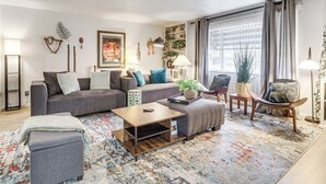 Un salon moderne comprenant un canapé, un pouf, une table basse et des objets décoratifs.