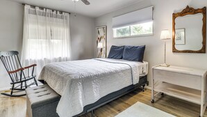 Une chambre à coucher comprenant un lit, un fauteuil à bascule, une table de chevet, une lampe, un ventilateur de plafond et une fenêtre avec des stores.