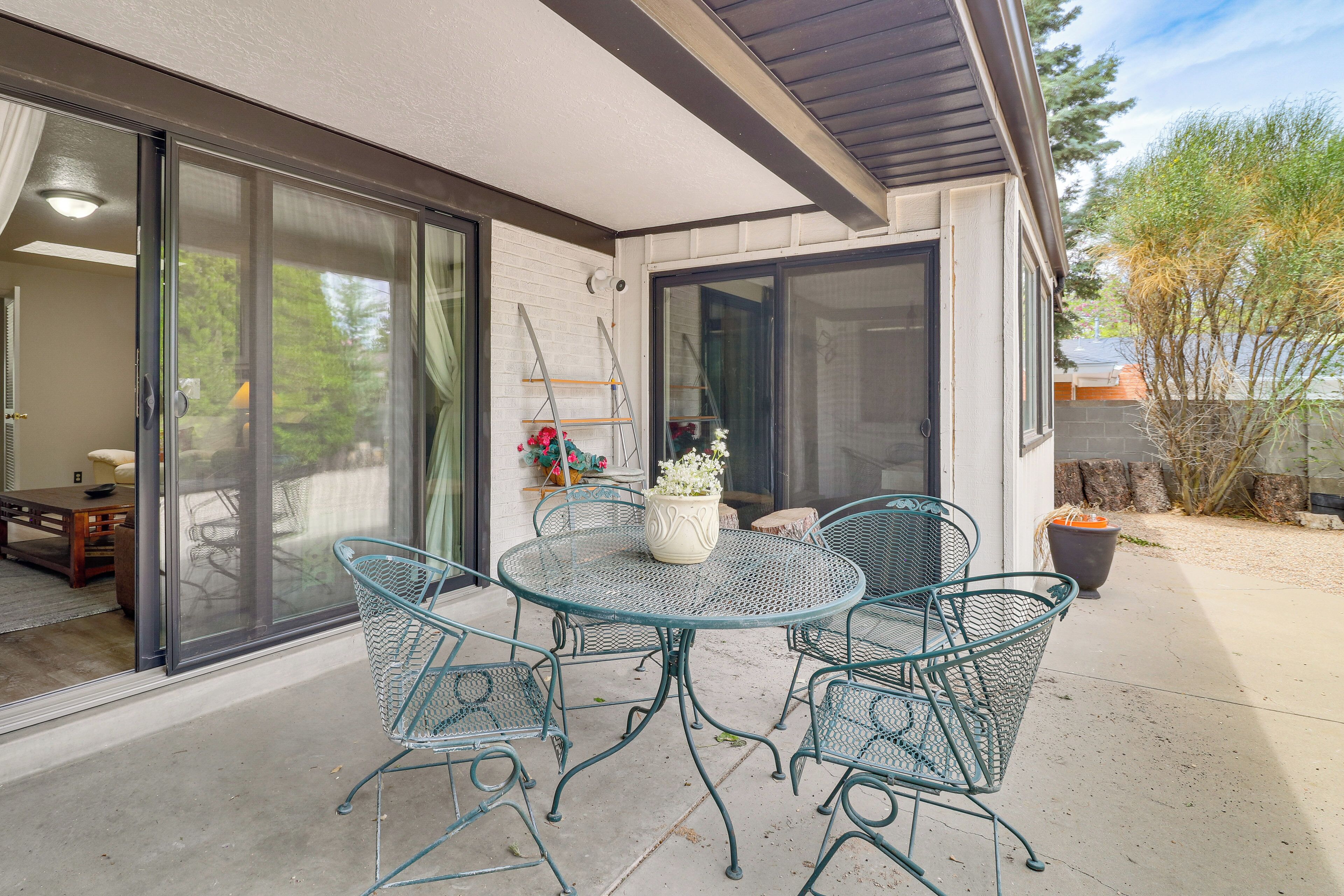 Une terrasse avec une table ronde et des chaises, un pot de fleurs et une porte-fenêtre coulissante donnant sur un espace intérieur.