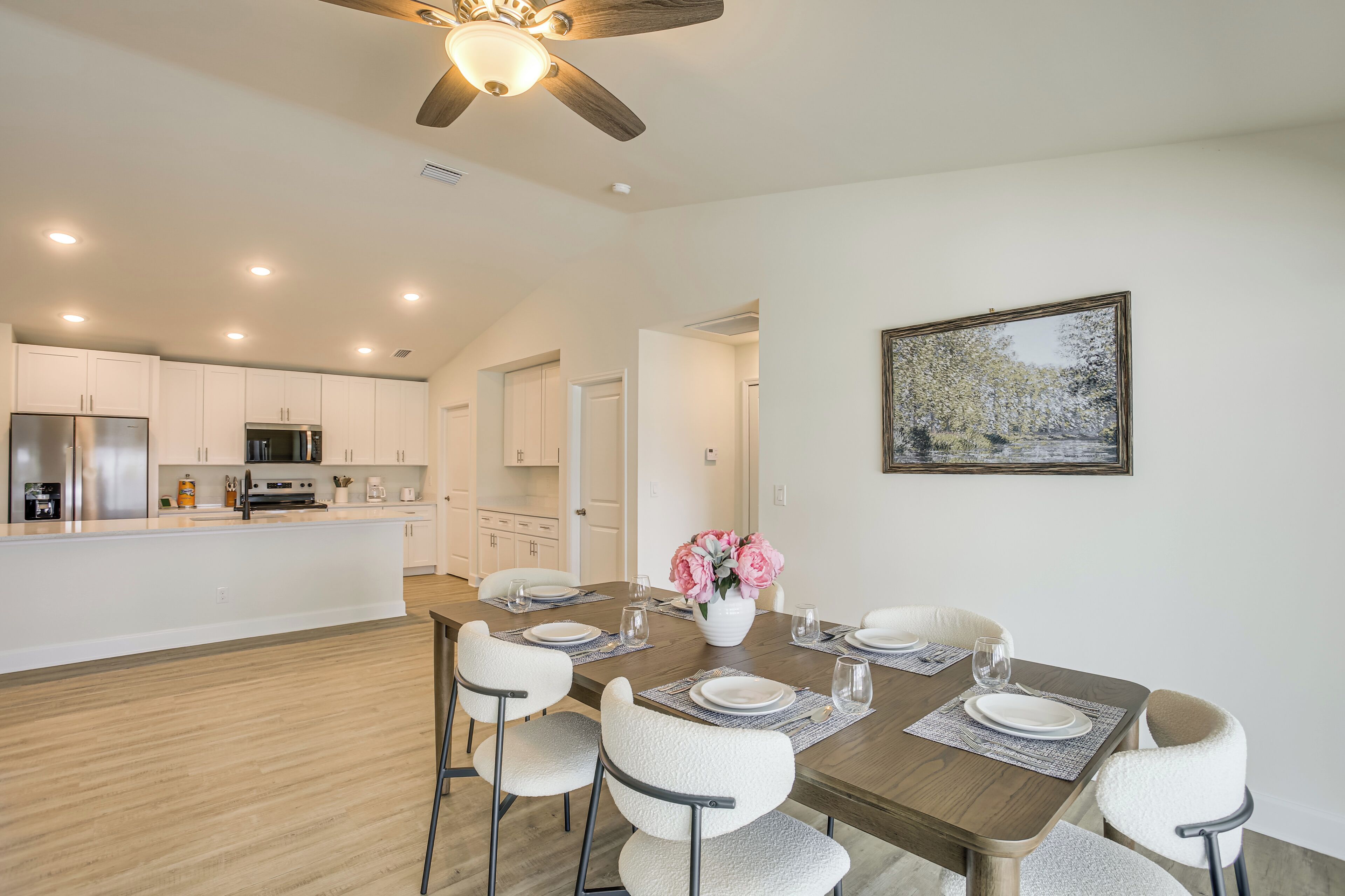 A dining area with a wooden table, white chairs, a vase of flowers, and a painting on the wall.