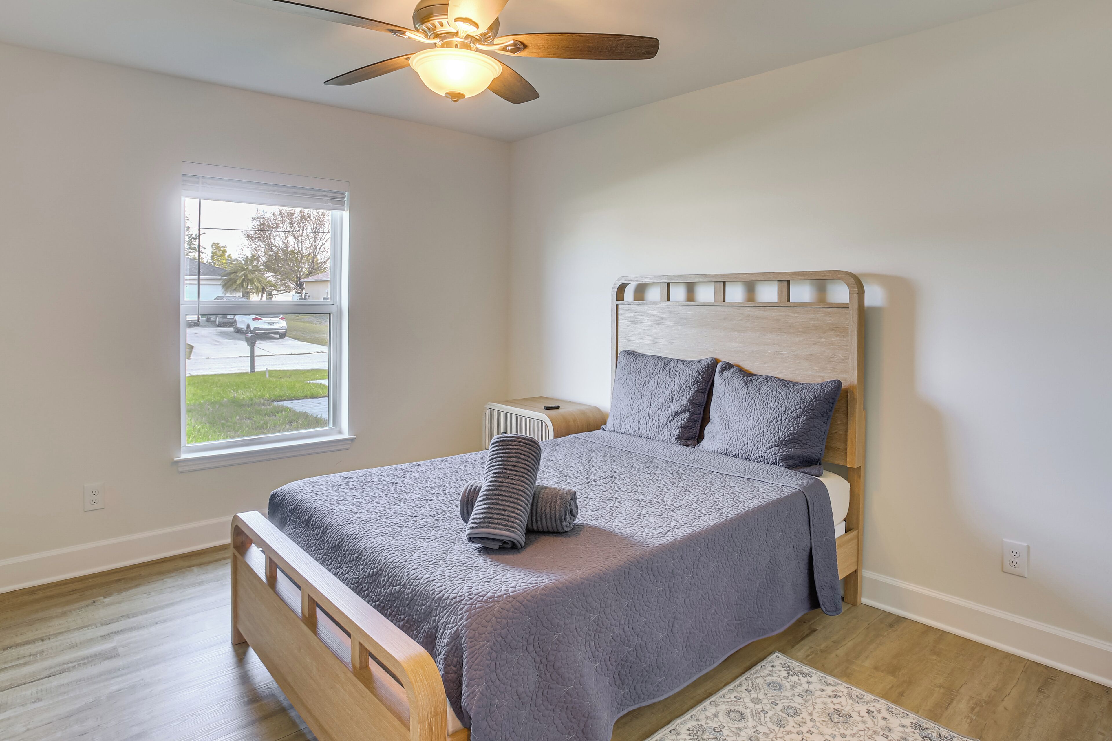 Une chambre à coucher avec un lit, un ventilateur de plafond, une fenêtre et une table de chevet.