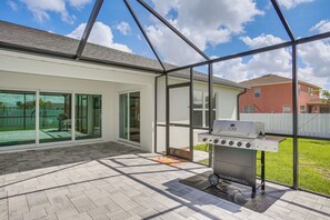 Eine überdachte Terrasse mit Grill, Glastüren zum Gleiten und Blick auf einen Garten.