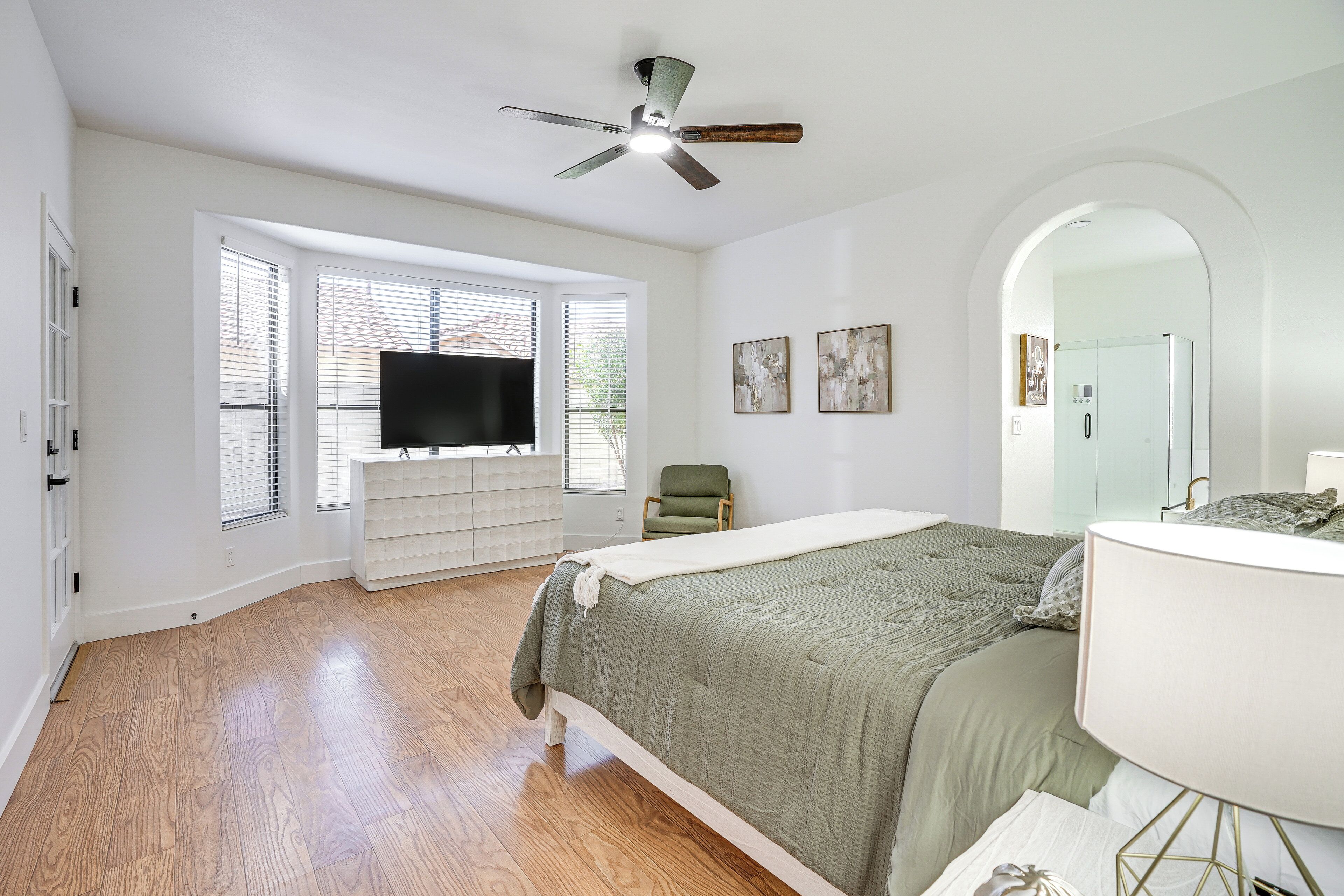 A bedroom with a bed, a TV, a ceiling fan, a window, and a door.