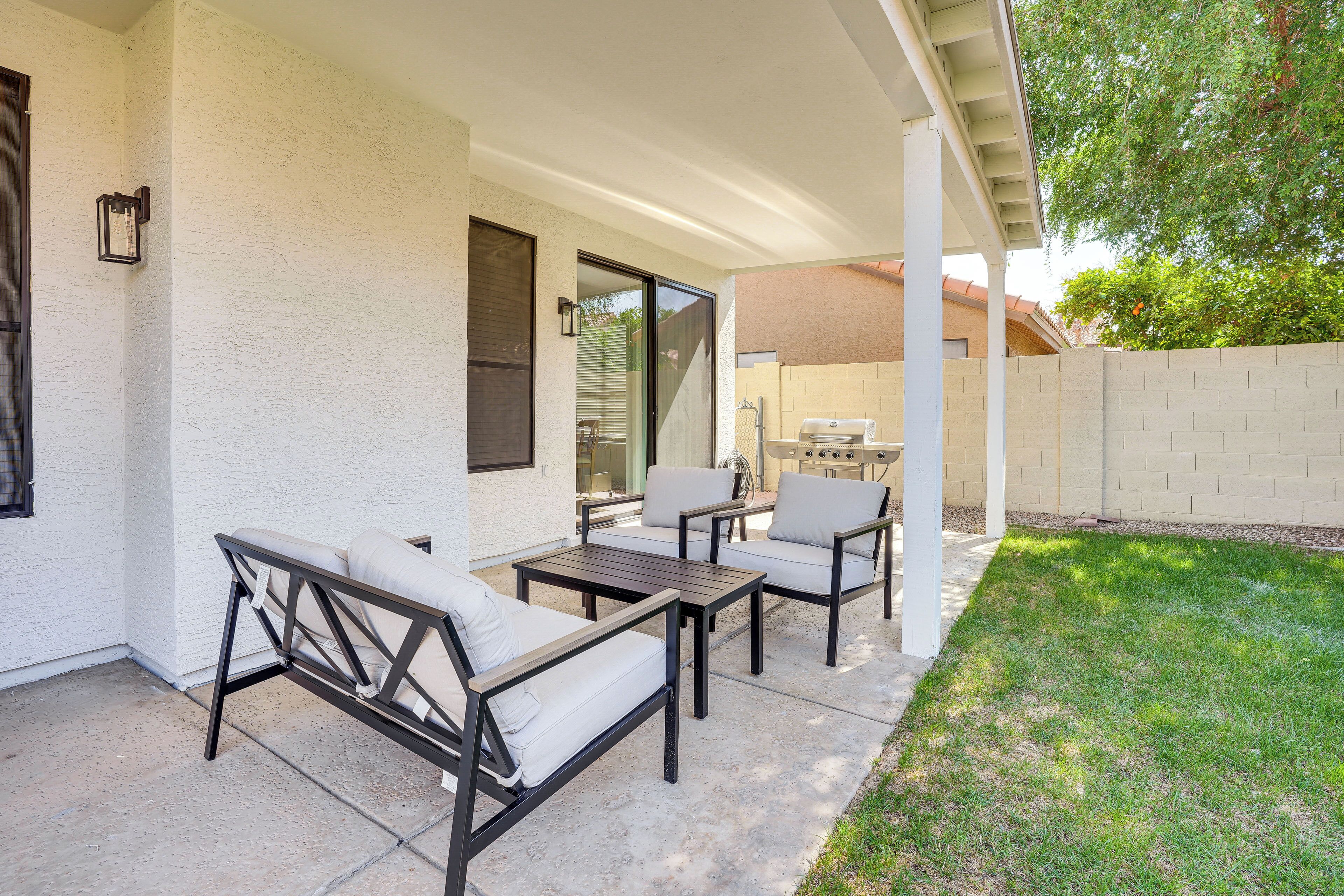 An outdoor patio with a covered seating area, a barbecue grill, and a white exterior wall.