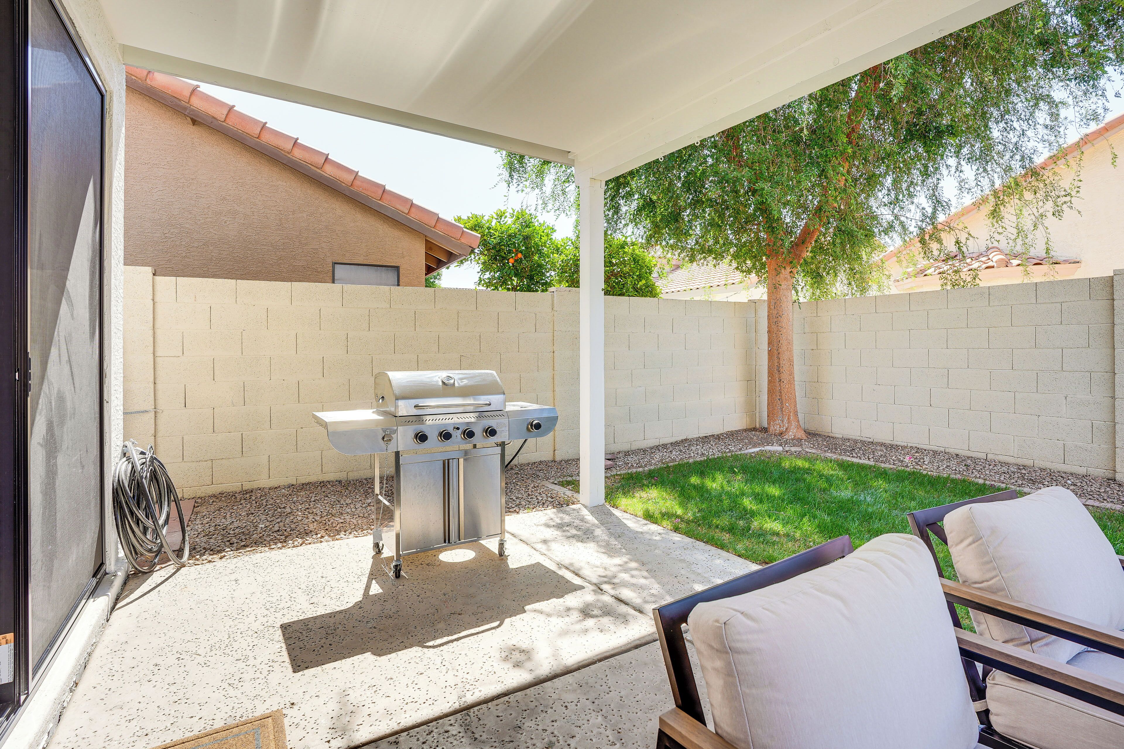 A covered patio area with a grill, a chair, and a small lawn.